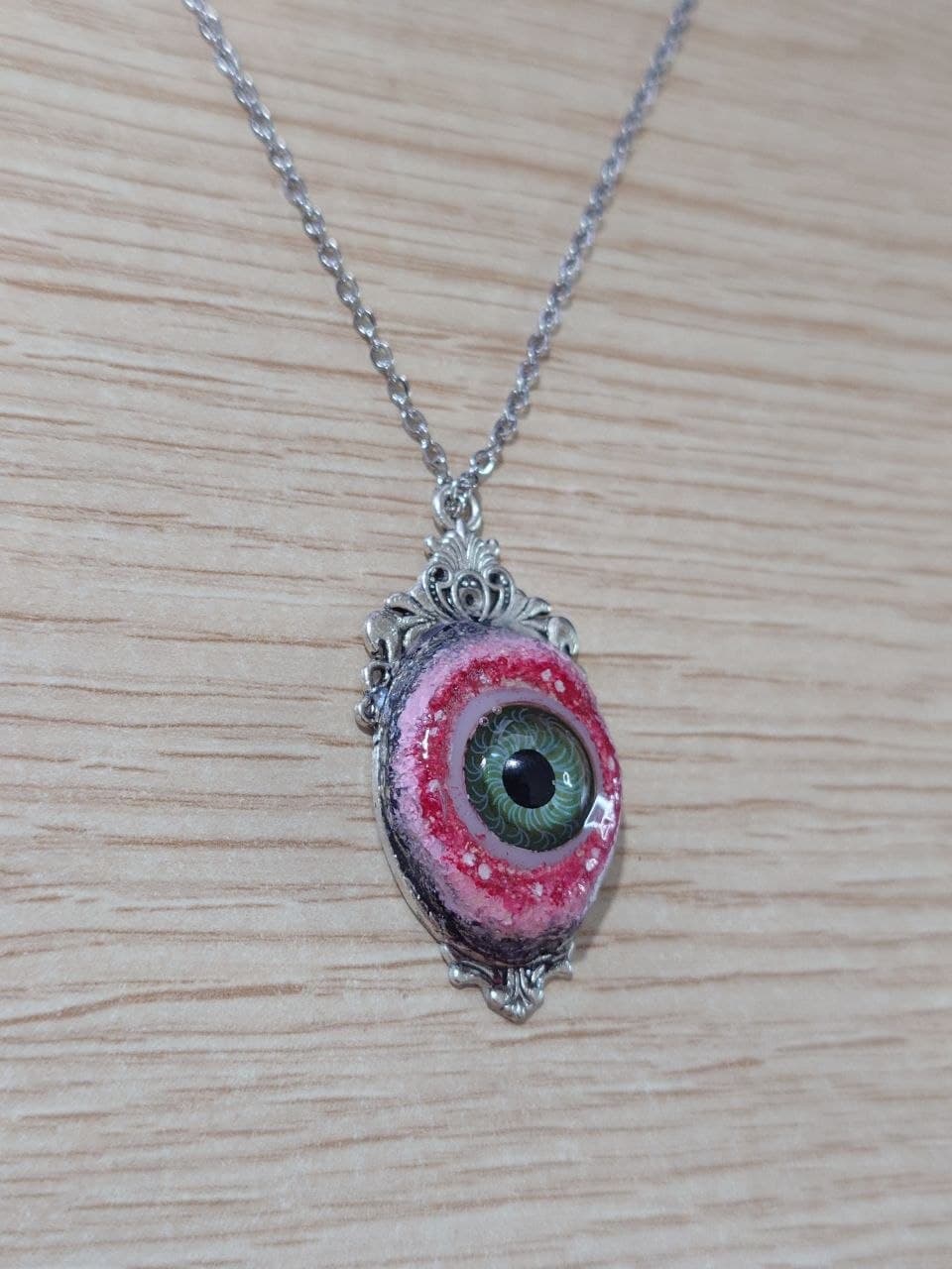 Collar artesanal ovalado con ojo verde y marco plateado, vista en ángulo