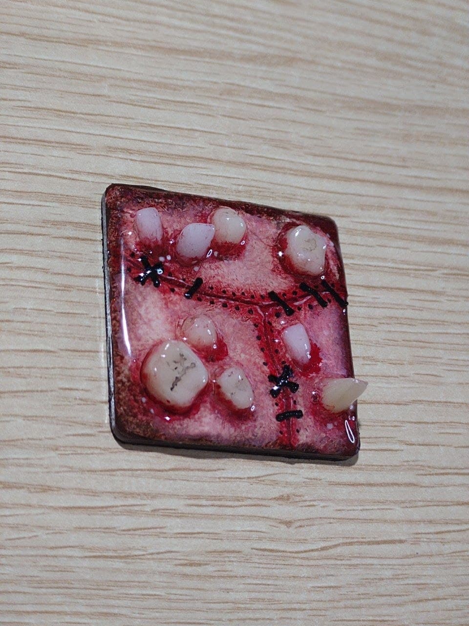 Imán artesanal de teratoma cosido en tonos rojos, vista en ángulo