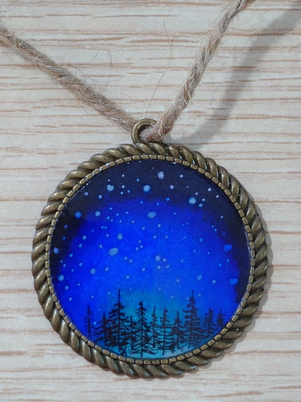 Collar artesanal con escena de bosque azul y marco dorado, detalle